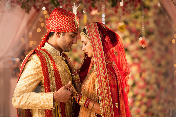 A newlywed bride and groom in traditional Indian wedding attire, looking at each other lovingly. A newlywed bride and groom in traditional Indian wedding attire, looking at each other lovingly.