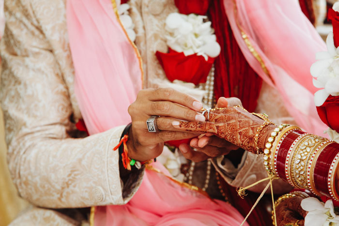 Close-up of a groom placing a wedding ring on his bride's finger, showcasing traditional Indian attire and henna. Close-up of a groom placing a wedding ring on his bride's finger, showcasing traditional Indian attire and henna.