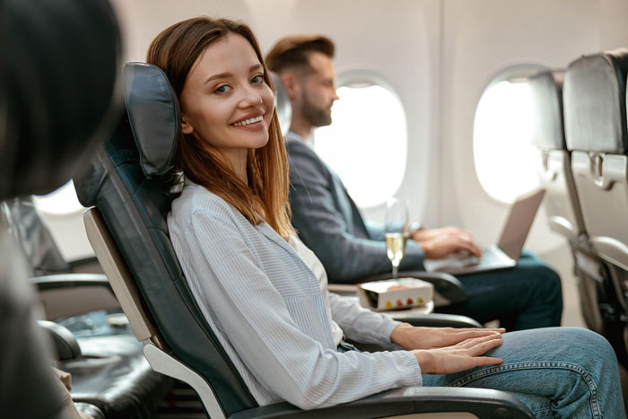 Woman smiling in a comfortable airplane seat after upgrading flight tickets for a family trip. Woman smiling in a comfortable airplane seat after upgrading flight tickets for a family trip.