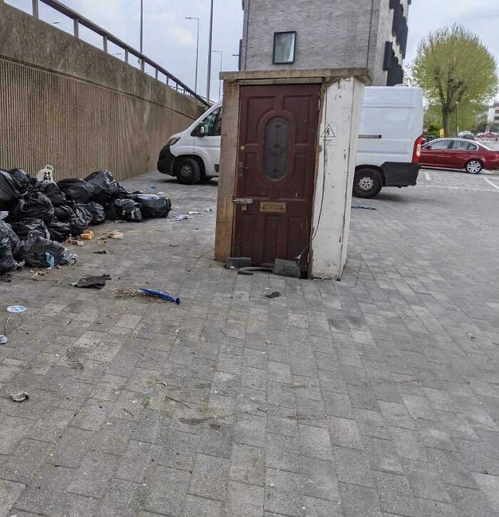 A freestanding wooden door in a parking lot next to black trash bags, exemplifying British humor.