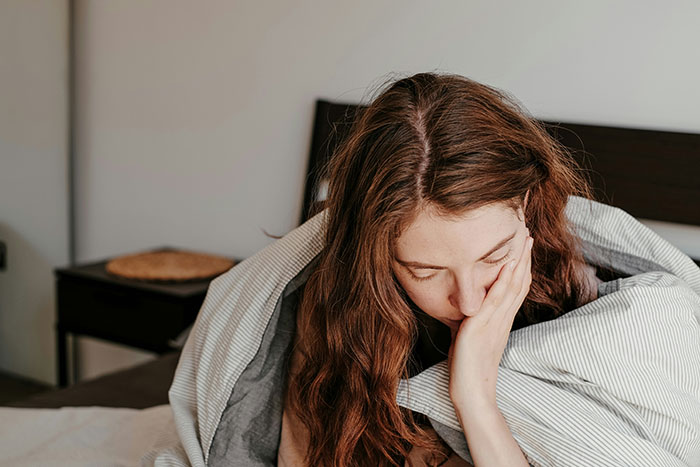 A woman looking distressed, head in hand, under a blanket, illustrating the emotional impact of wife's jealousy.