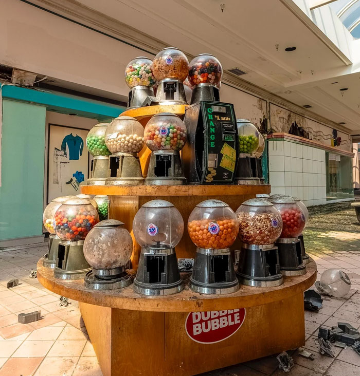 A cluster of old gumball machines with colorful candy, standing in an abandoned mall, exploring unexpected finds.