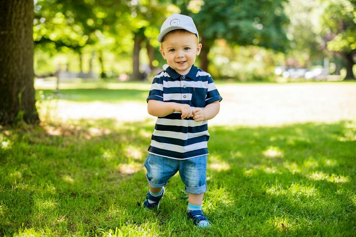 A smiling toddler wearing a cap and striped shirt in a park, related to the difficulty of pronouncing a common name. A smiling toddler wearing a cap and striped shirt in a park, related to the difficulty of pronouncing a common name.