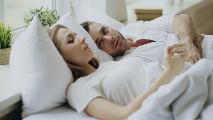 College life: A couple in bed, the man looking concerned, depicting the new world and realities of college relationships.