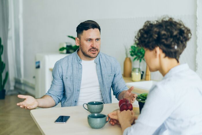 A man sitting at a table gestures while talking to his girlfriend during a serious conversation.