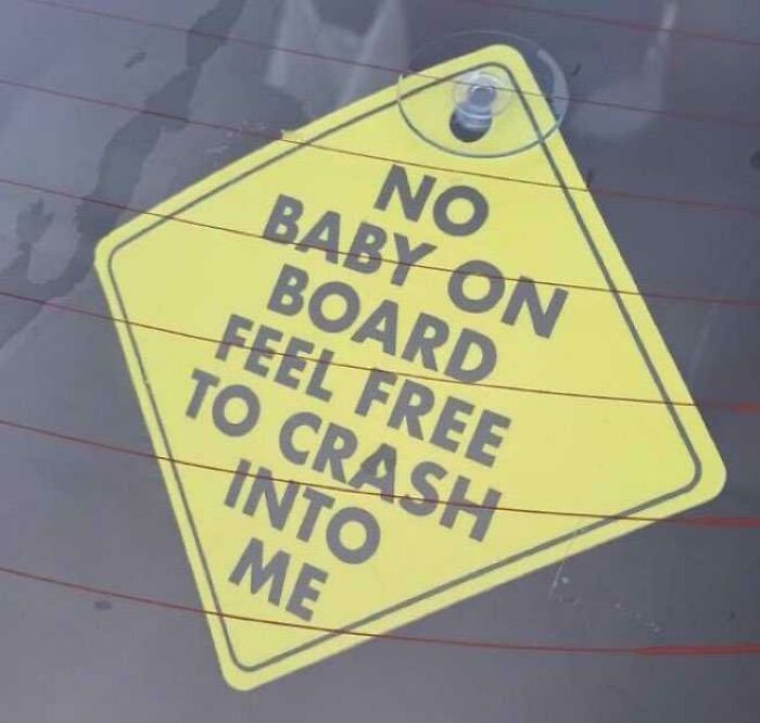 A yellow car sign that reads NO BABY ON BOARD FEEL FREE TO CRASH INTO ME, an example of dry British humor.