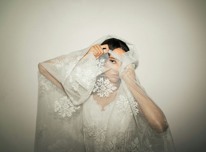 A woman partially obscured by a white, delicate lace fabric, symbolizing the hidden aspects and control within cults.