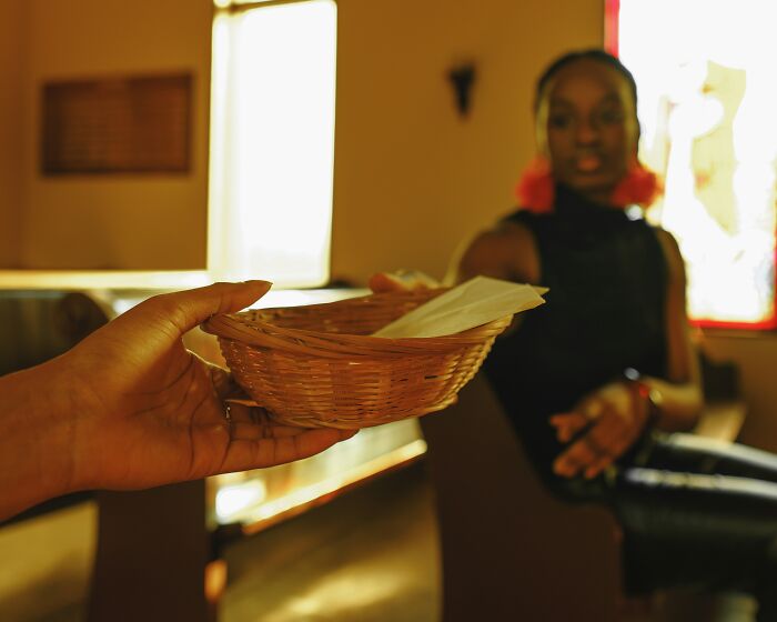 A hand extends a woven basket, possibly for offering, to a person seated in a church, symbolizing escaping cults.