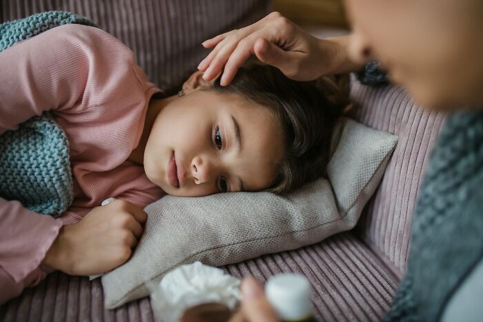 A sick child lies in bed with a hand on her forehead, symbolizing the health issues faced by people who escaped cults.