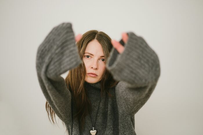 A woman in a grey sweater with outstretched arms, representing the experiences of people who escaped cults.
