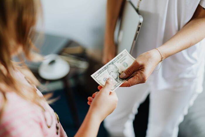 A hand giving a 10 dollar bill to another hand, illustrating financial manipulation often seen in cults.