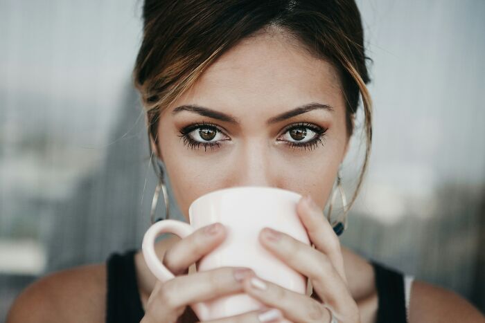 A woman with intense eyes sips from a pink mug, reflecting on the disturbing things people who escaped cults share.