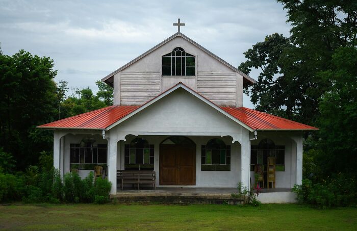 An exterior view of a simple white church with a red roof and a cross, related to stories of escaping cults.