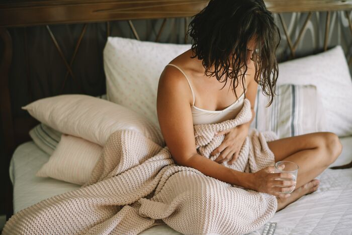 A distressed woman sitting on a bed with a blanket, possibly struggling with the aftermath of cults and ADHD.