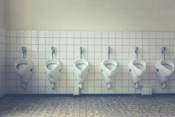 A row of six white urinals in a public restroom, metaphorically relating to disturbing things no one questions in cults.