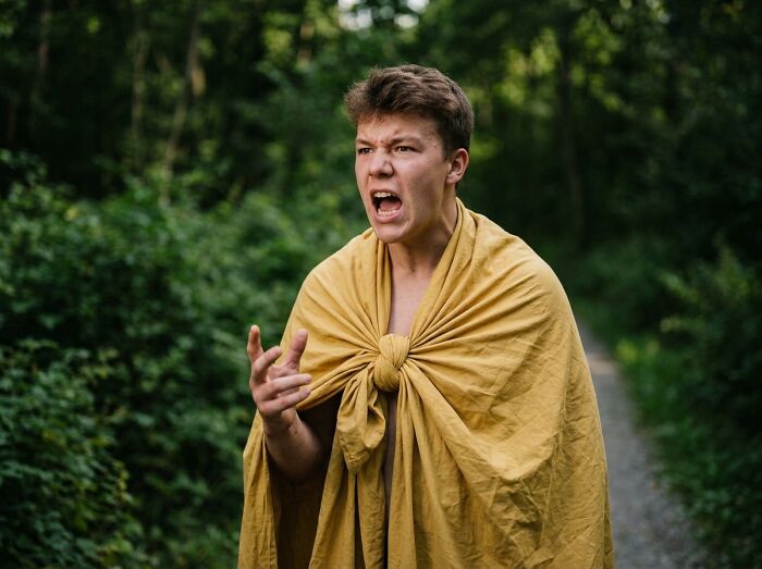 A young man in a yellow cloak, shouting in a forest, experiencing the freedom of college life.