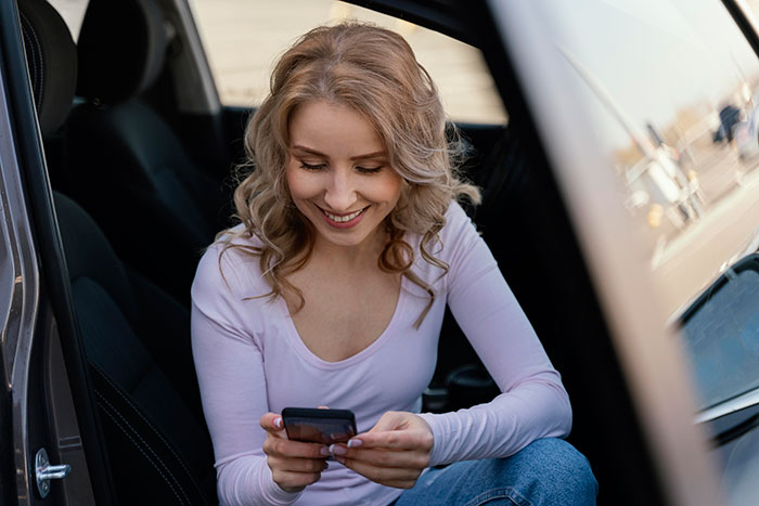 Blonde woman sitting in a car, smiling while looking at her phone, possibly engaged in secret conversations. Blonde woman sitting in a car, smiling while looking at her phone, possibly engaged in secret conversations.
