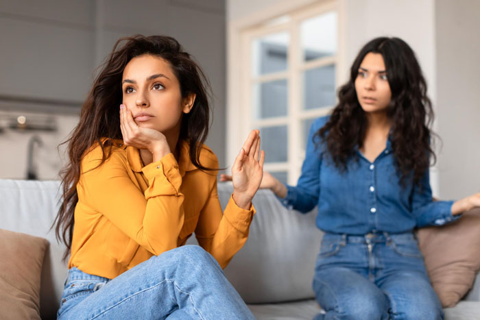 Two women, one looking annoyed and holding up a hand, discussing kid's education and wardrobe rights.