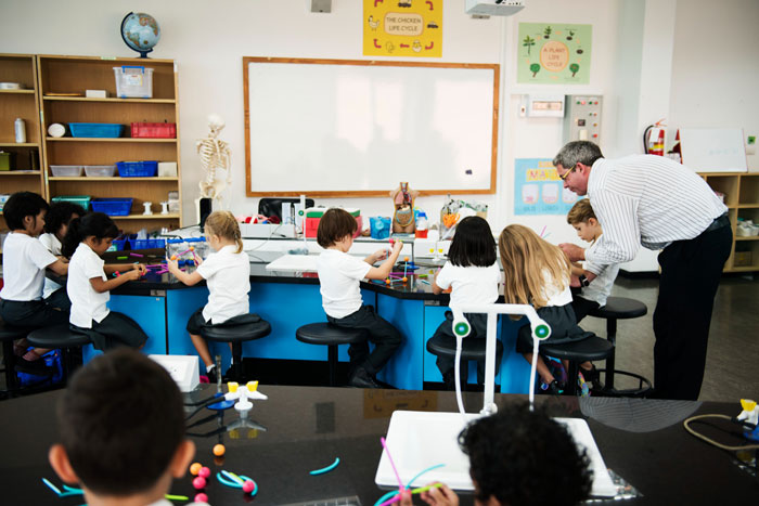 A classroom filled with young students engaged in an education activity, with a teacher supervising.