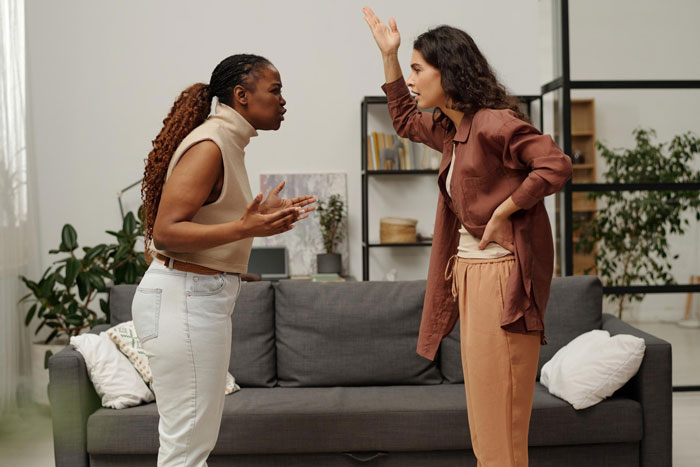 Two women arguing, one gesturing emphatically, representing a disagreement about kid's education and wardrobe rights.