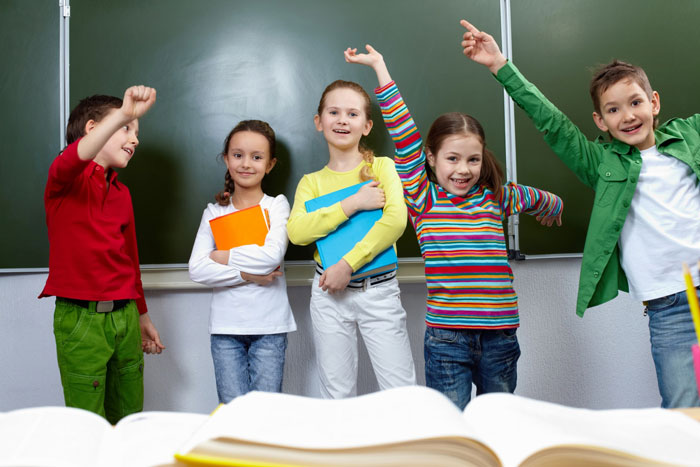 Happy children raise their hands in a classroom, symbolizing the importance of a kid's education.