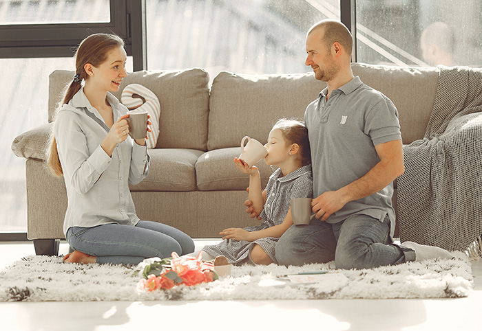 Family enjoying miscommunication and checking baby cam in their living room. Husband, wife, and child share drinks.