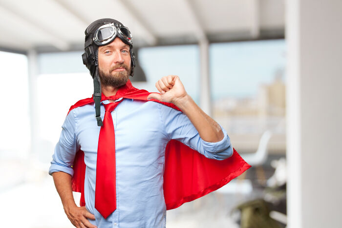 A man dressed as a superhero with a red cape and pilot's helmet, pointing to himself, embodying an epic comeback.