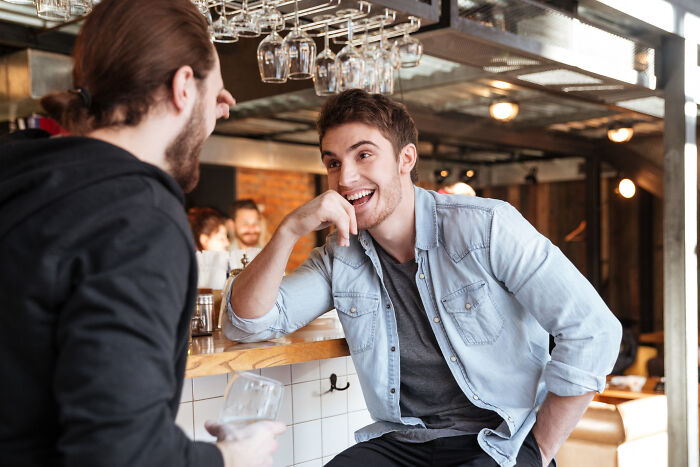 Two men sharing an epic comeback, laughing at a bar, showcasing their wit and humor.