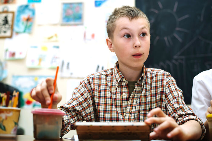 A boy in a plaid shirt painting, looking up thoughtfully, perhaps imagining epic comebacks.