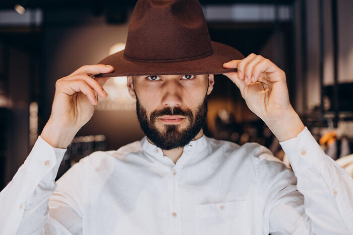 A man with a beard adjusting a brown hat, looking directly at the camera. He is wearing a white shirt. Epic comebacks.