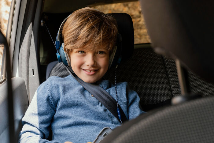 A young boy wearing headphones and a seatbelt in a car, smiling, possibly listening to stories of epic comebacks.