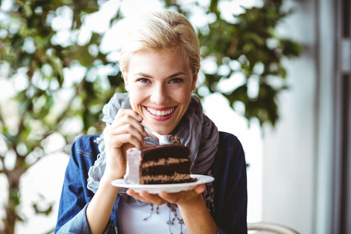 A woman smiling while holding a slice of chocolate cake, celebrating an epic comeback.