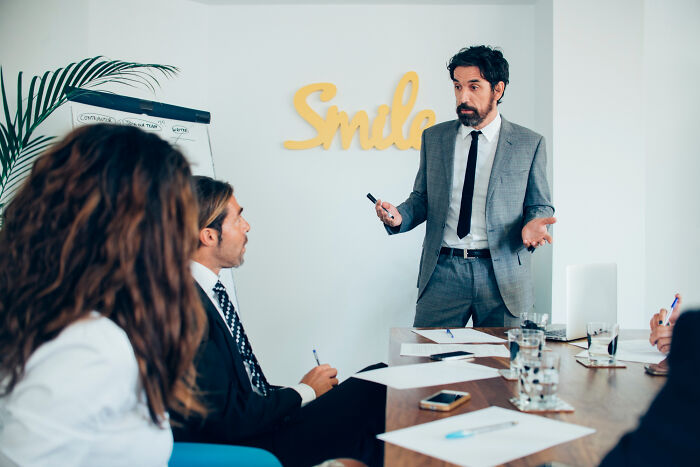 A man in a suit presenting to colleagues, possibly delivering an epic comeback in a meeting.