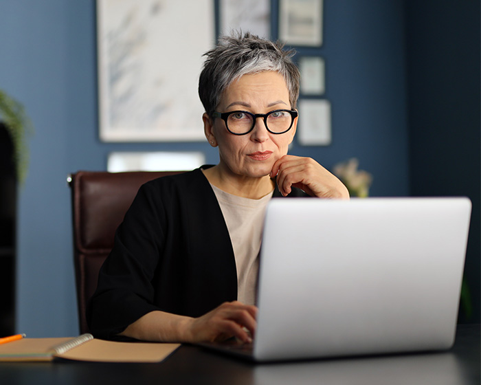 An older woman with glasses working on a laptop, using the resume botoxing trick to get a job.