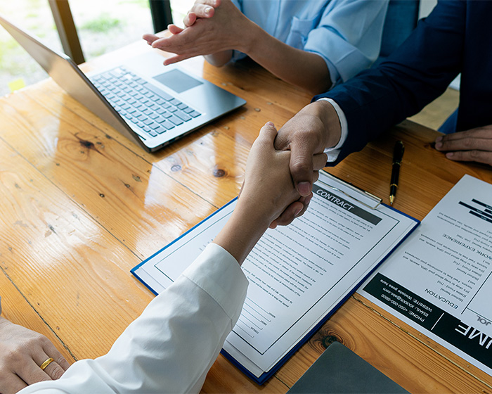 Two people shaking hands over a contract and resume, symbolizing successful job applications and career advancement.