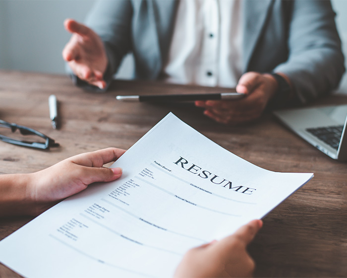 A person holding a resume during a job interview, illustrating the 'resume Botoxing' trick for job seekers.