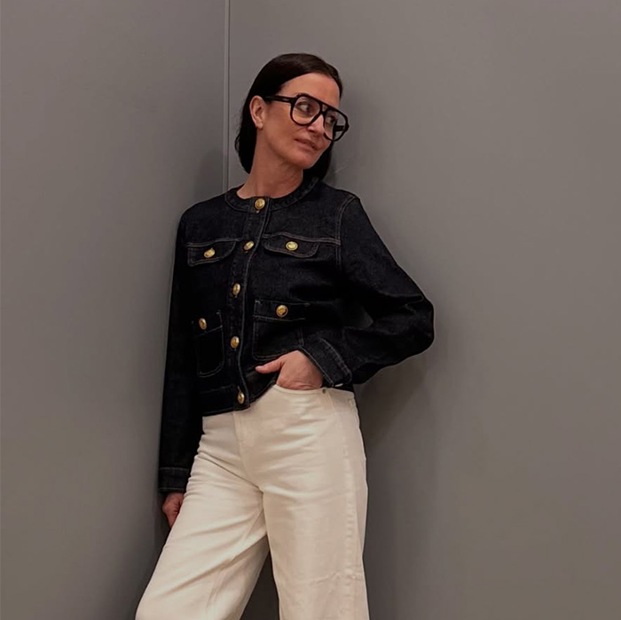 A stylish 52-year-old woman in glasses and a denim jacket, embodying the confidence from a resume botoxing trick.