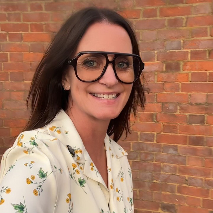 A 52-year-old woman in large glasses smiling against a brick wall, revealing her resume botoxing trick.
