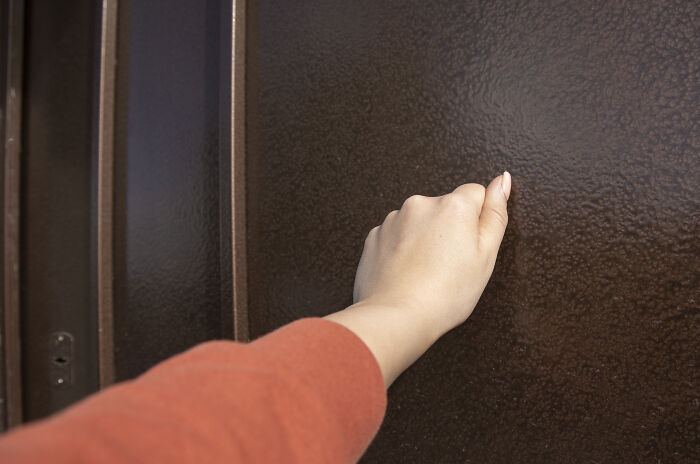 A hand knocking on a dark brown door, symbolizing a house rule about privacy or entering rooms.