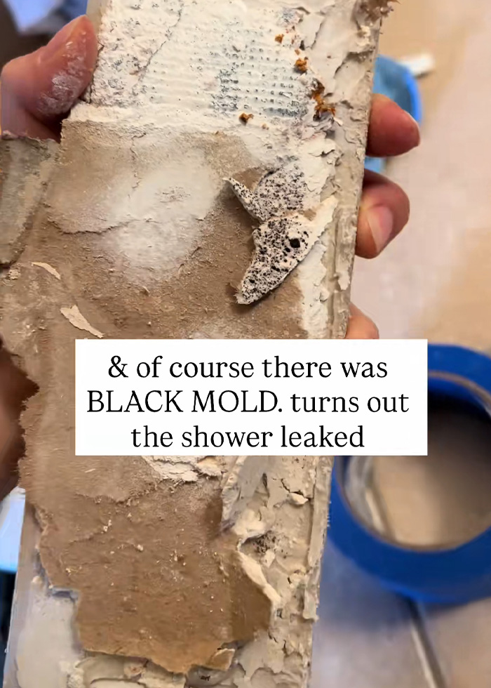 A hand holding up a piece of a bathroom wall, showing black mold from a shower leak, causing unexplained symptoms. A hand holding up a piece of a bathroom wall, showing black mold from a shower leak, causing unexplained symptoms.