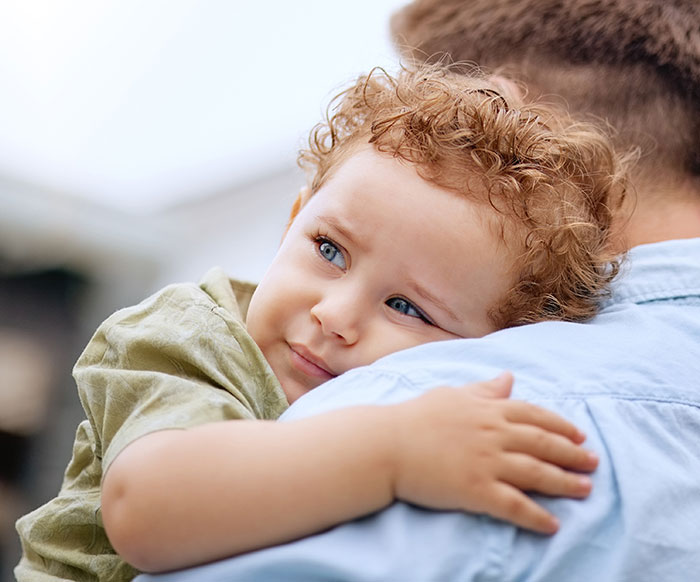 A young, curly-haired orphaned nephew is held by an adult, symbolizing the discussion of primary caregiver roles. A young, curly-haired orphaned nephew is held by an adult, symbolizing the discussion of primary caregiver roles.