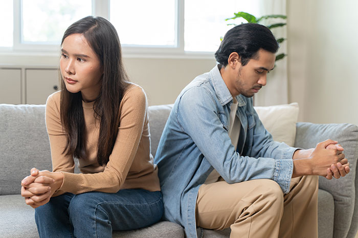 A couple sits back-to-back on a couch, looking upset, relating to a wife refusing to be a primary caregiver. A couple sits back-to-back on a couch, looking upset, relating to a wife refusing to be a primary caregiver.