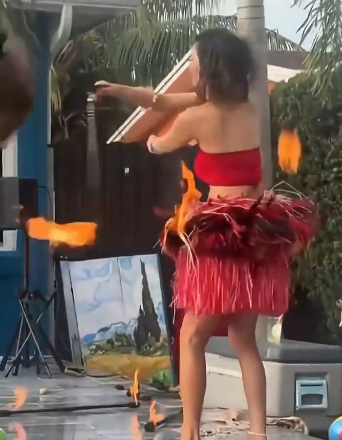 A woman performing with fire, her skirt catching fire mid-performance, with flames visible around her waist. A woman performing with fire, her skirt catching fire mid-performance, with flames visible around her waist.