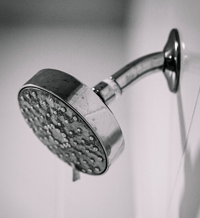 A close-up, black and white image of a shower head, symbolizing the act of showering at home. A close-up, black and white image of a shower head, symbolizing the act of showering at home.