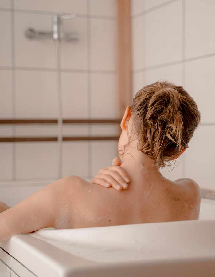 Woman in a bathtub, hand on her shoulder, with wet hair after showering at home, feeling pulling sensations. Woman in a bathtub, hand on her shoulder, with wet hair after showering at home, feeling pulling sensations.
