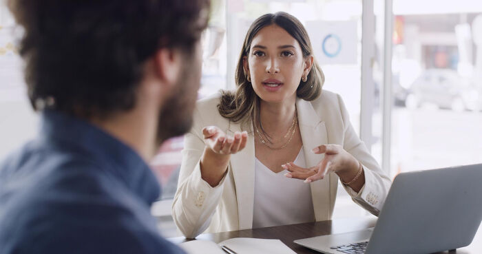 A woman gesturing while talking to a man in an office setting. Women's comments making men plan their escape.