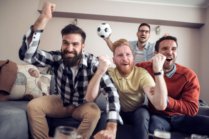 Men watching soccer, enthusiastically reacting, perhaps distracting themselves from comments or planning an escape.