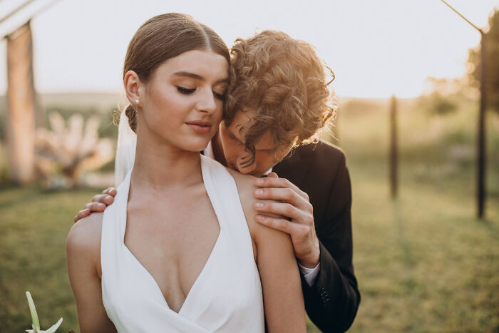 A man embracing a woman in a wedding dress, looking at her neck. Men planning their escape from date nights.