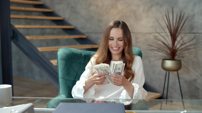 A woman happily counting money, reflecting discussions about women's finances and men's reactions.