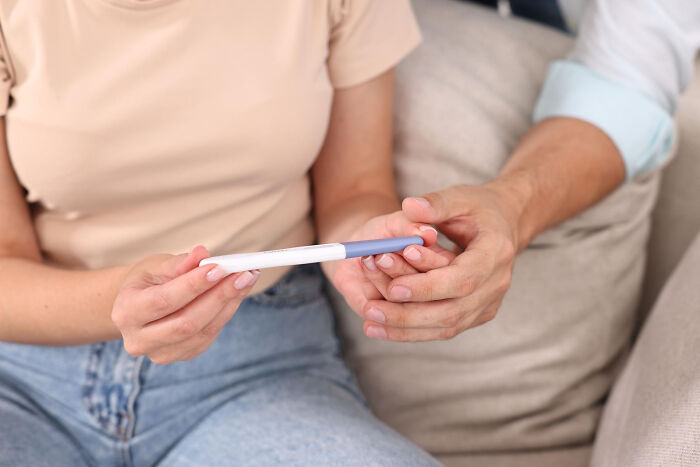 A couple holding a pregnancy test, showing a significant life event that can be influenced by women's comments.